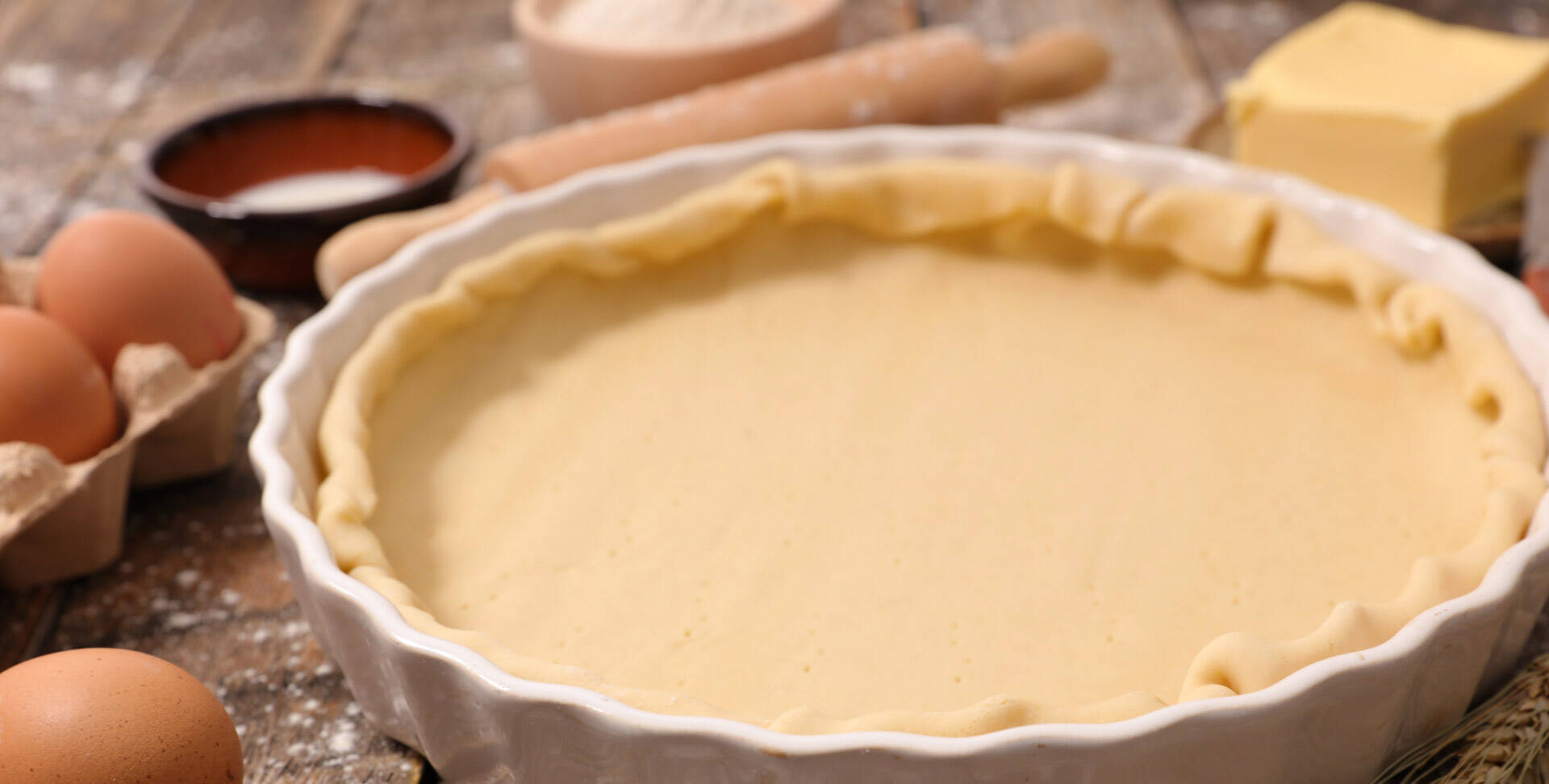 Un plat à tarte avec une pâte et des oeufs, de la farine